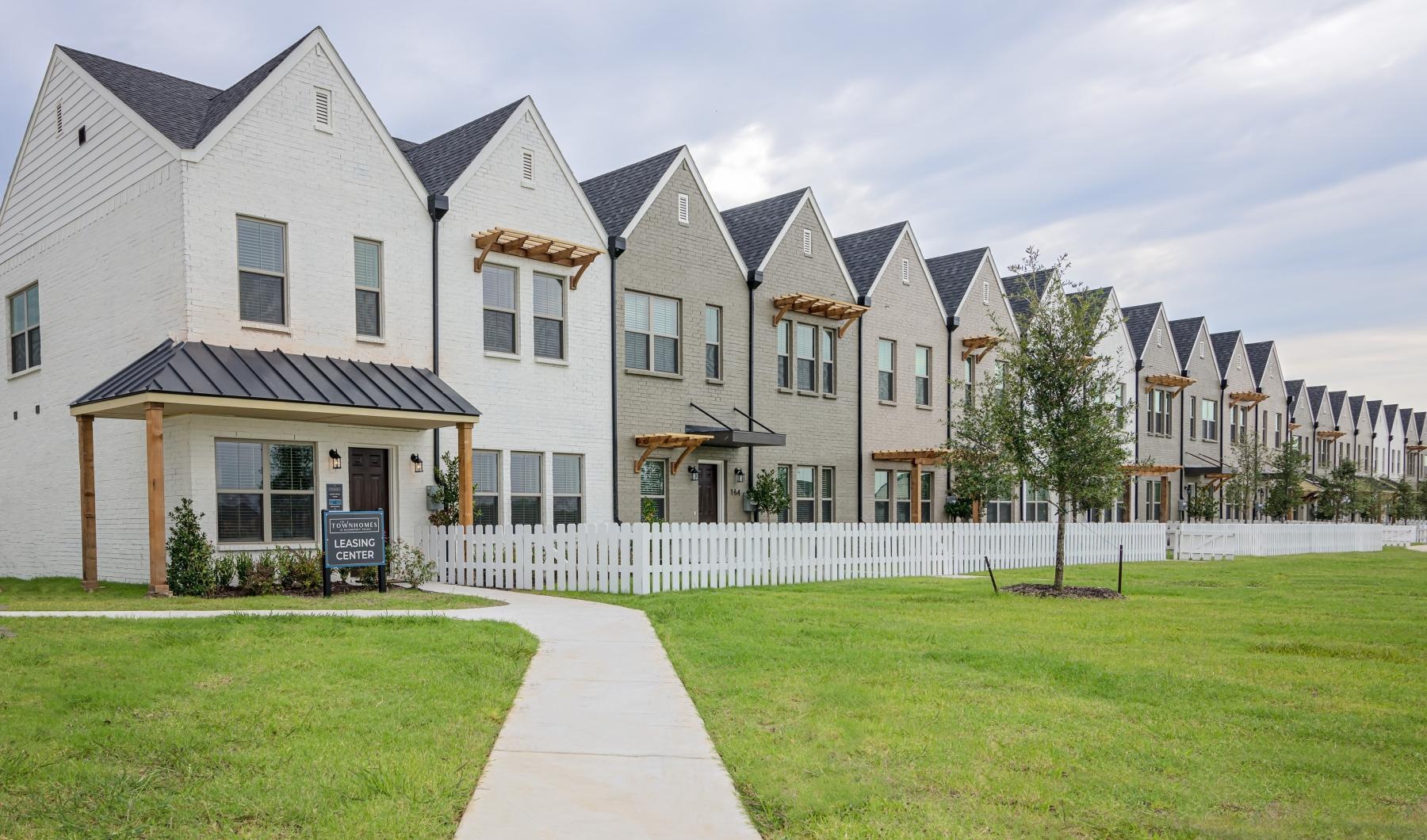 a row of townhomes with yards and a lawn and white picket fence