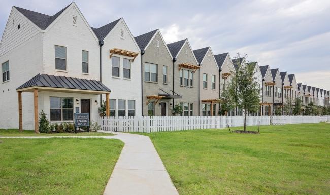 a row of townhomes with yards and a lawn and white picket fence