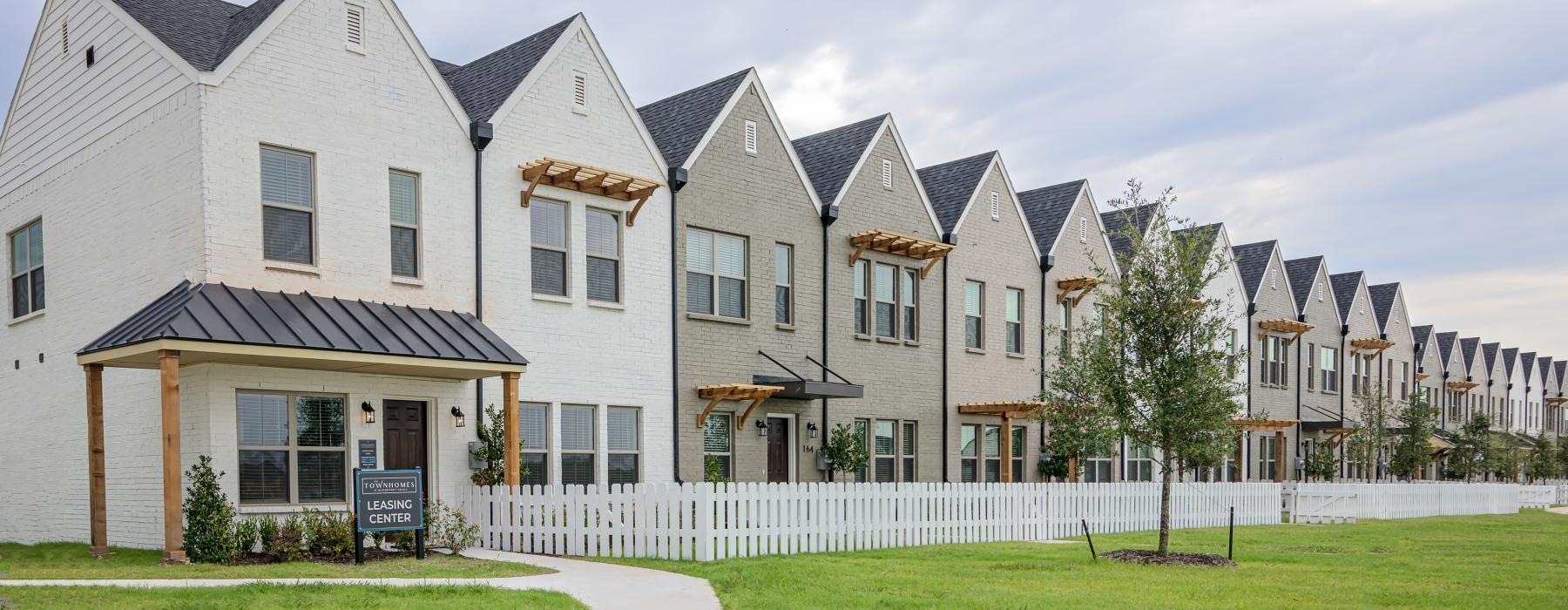 a row of townhomes with yards and a lawn and white picket fence
