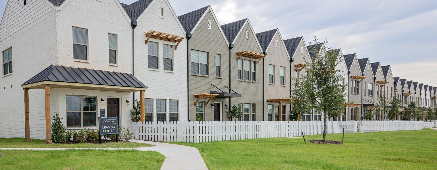 a row of townhomes with yards and a lawn and white picket fence